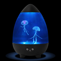 Lámpara de medusas Venotal sobre fondo negro: cuerpo ovoide transparente con agua azul iluminada, tapa cónica negra y base de tres patas.